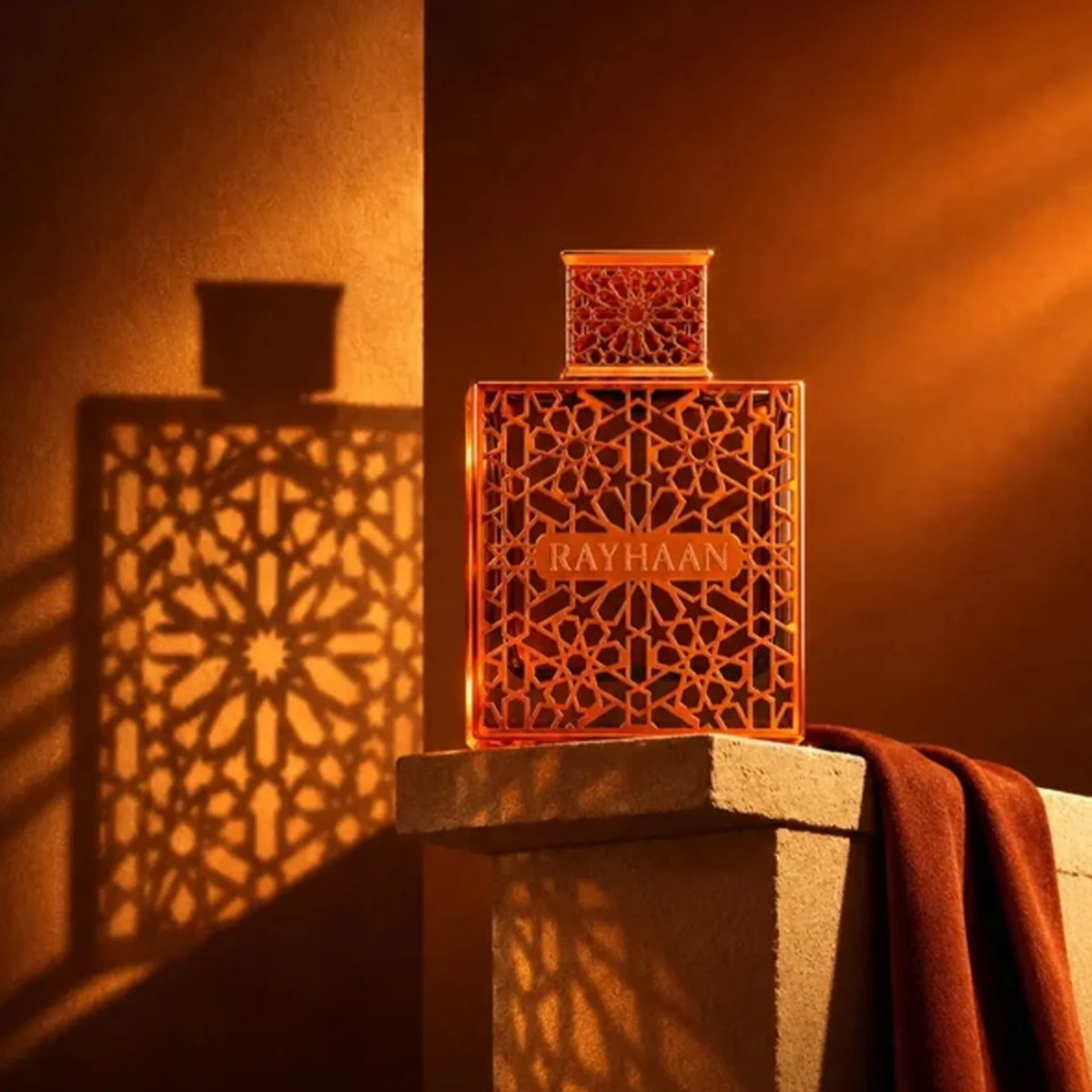 Rayhaan Vantage 100ml perfume bottle with intricate bronze geometric lattice casing on a stone pedestal in warm light.